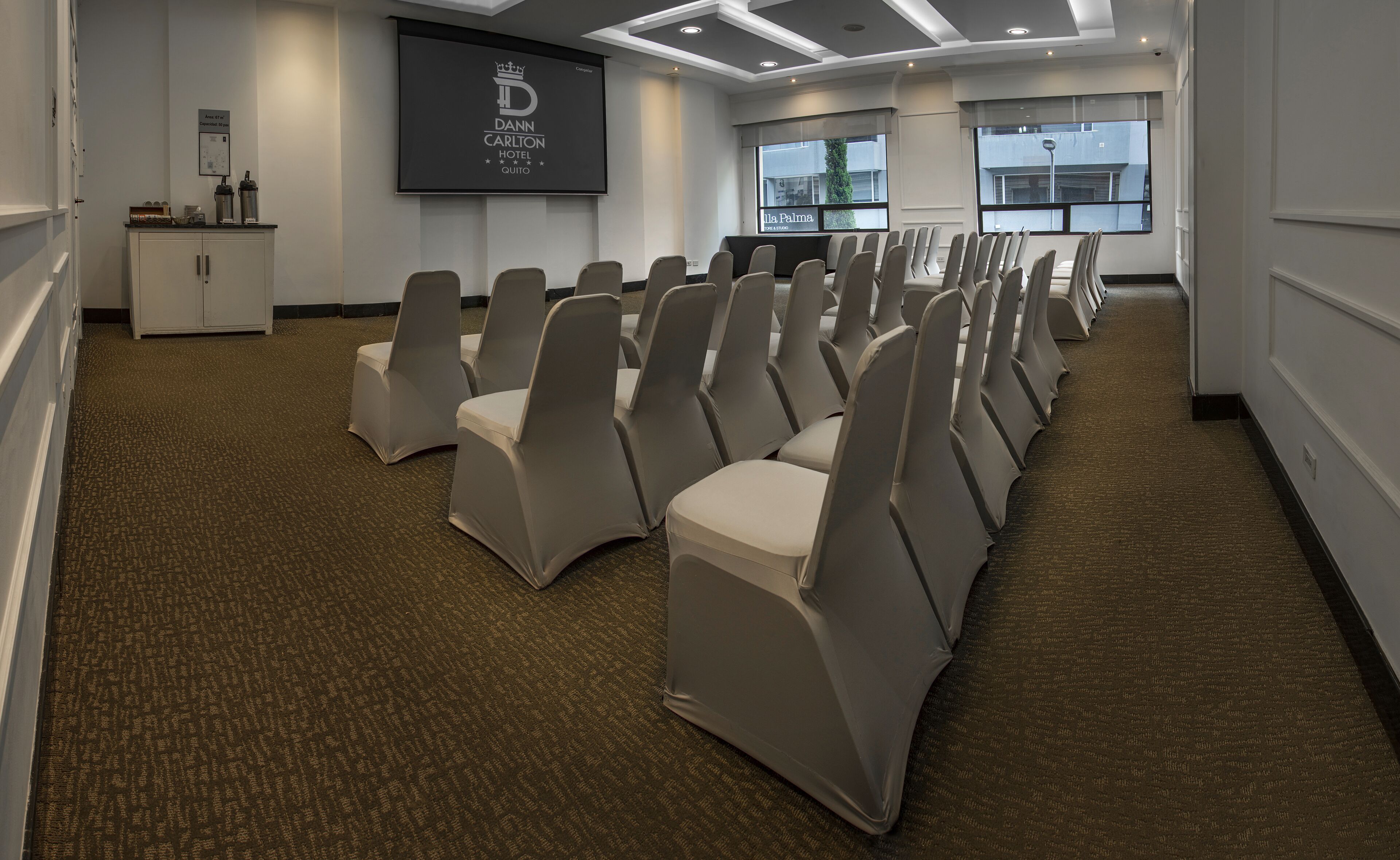 A conference room with rows of chairs, a podium, and a screen displaying the hotel name.