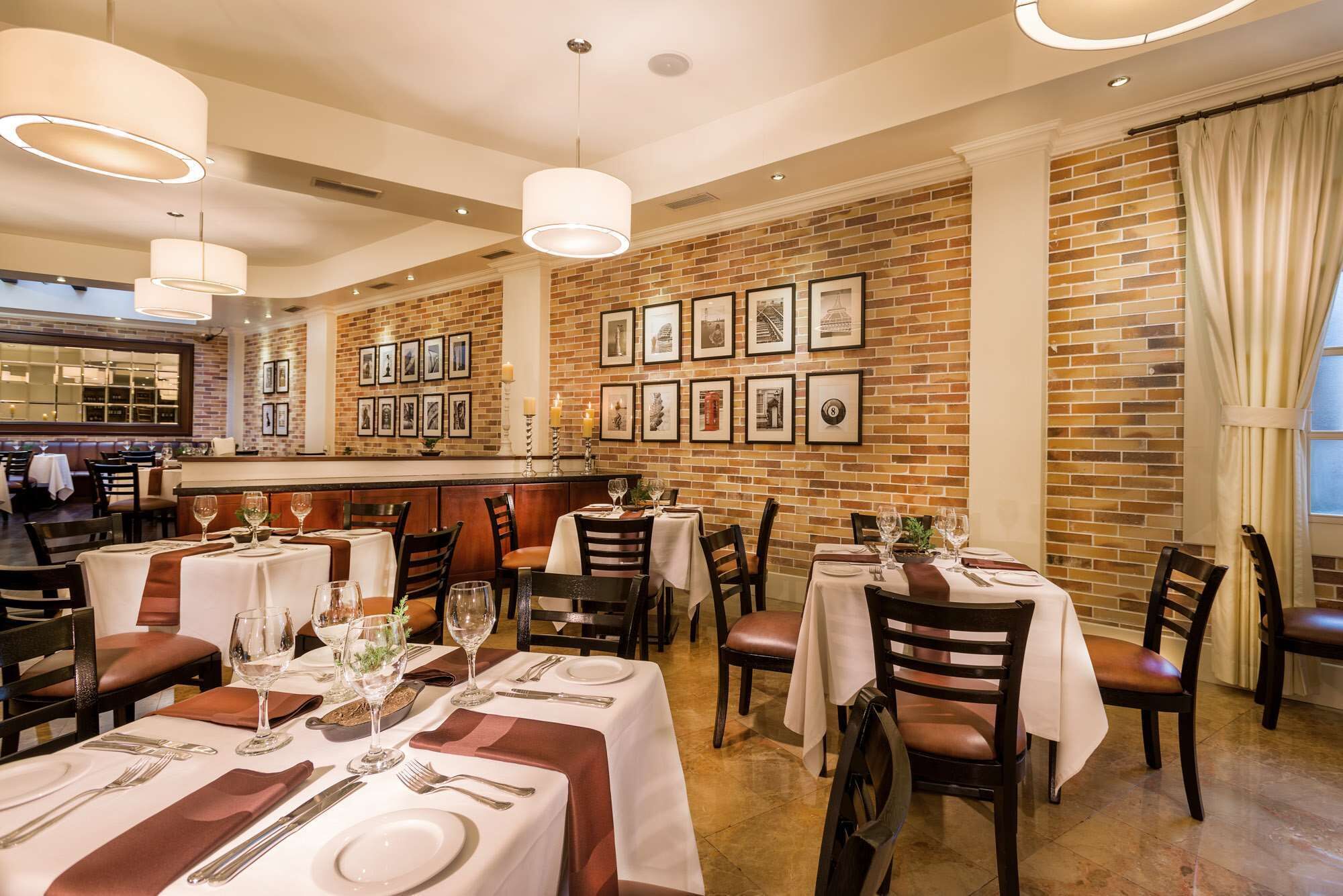 A restaurant with brick walls, framed pictures, and tables set for dining.