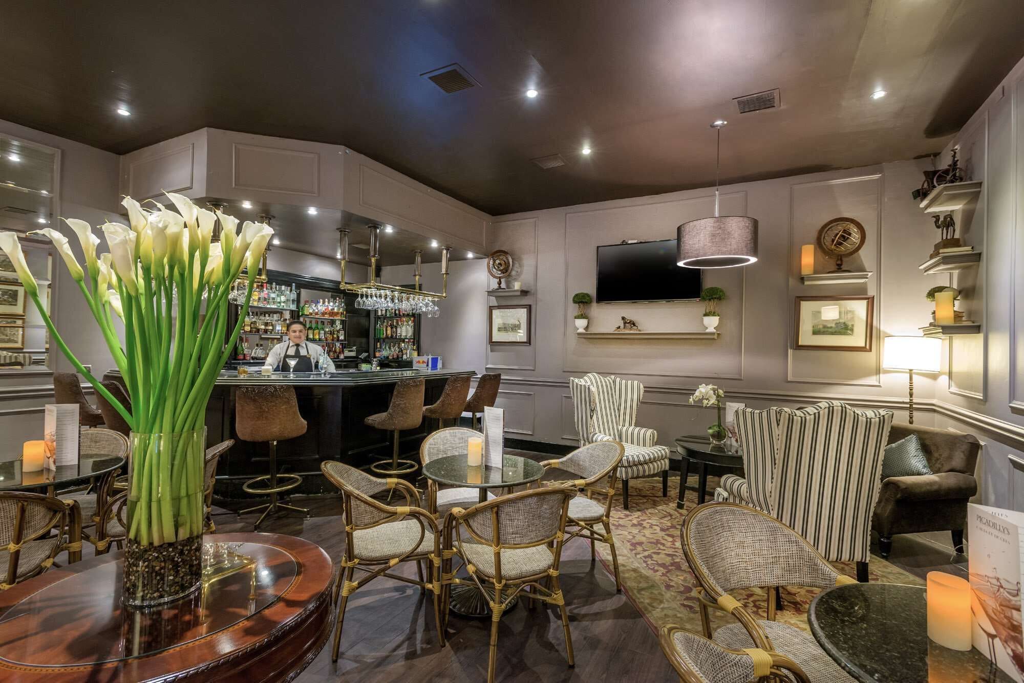 A bar area with wicker chairs, a round table, and a large vase of white flowers.