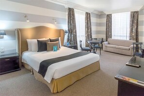 Una habitación de hotel con una cama grande, un sofá, una mesa de comedor y un televisor.