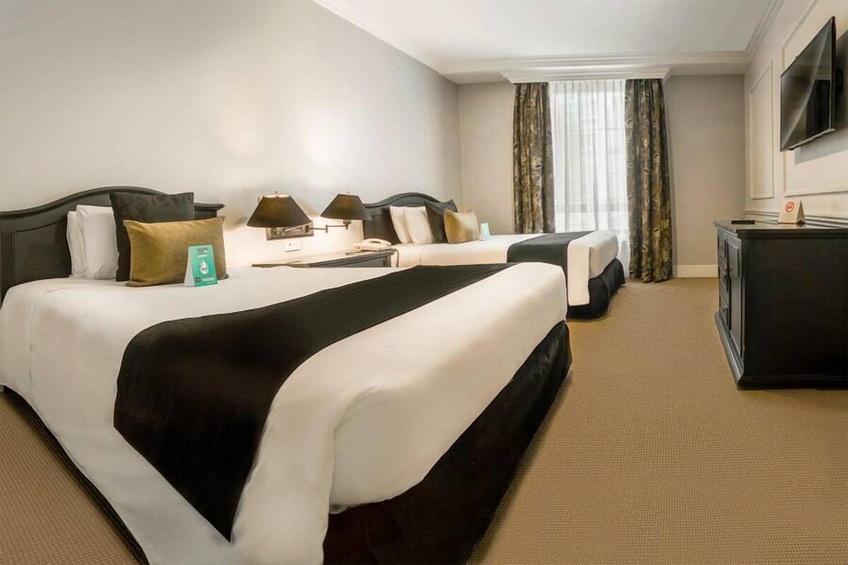A hotel room with two beds, a desk, a television, and a window with curtains.