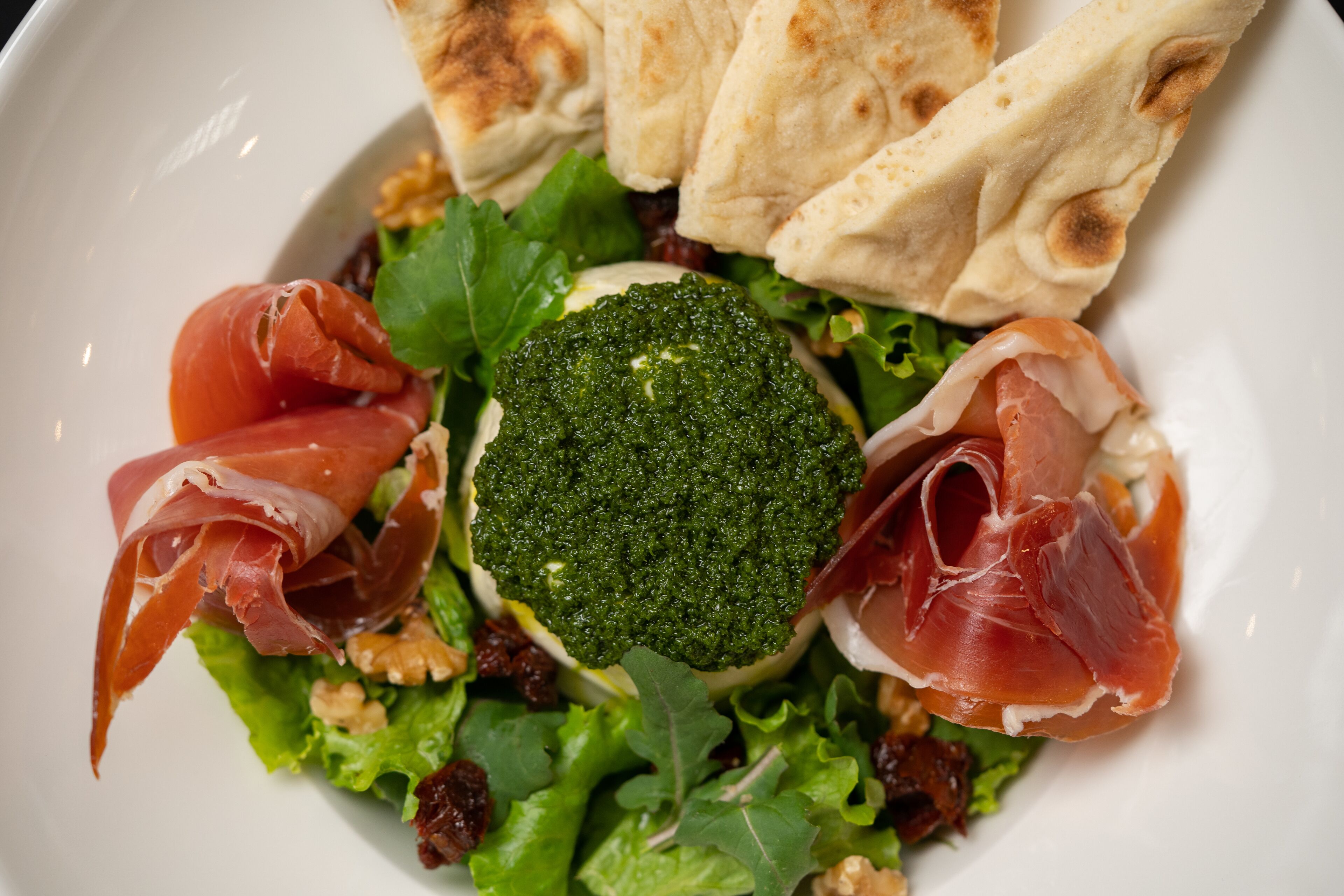 Un plato con ensalada de brócoli, prosciutto y nueces.