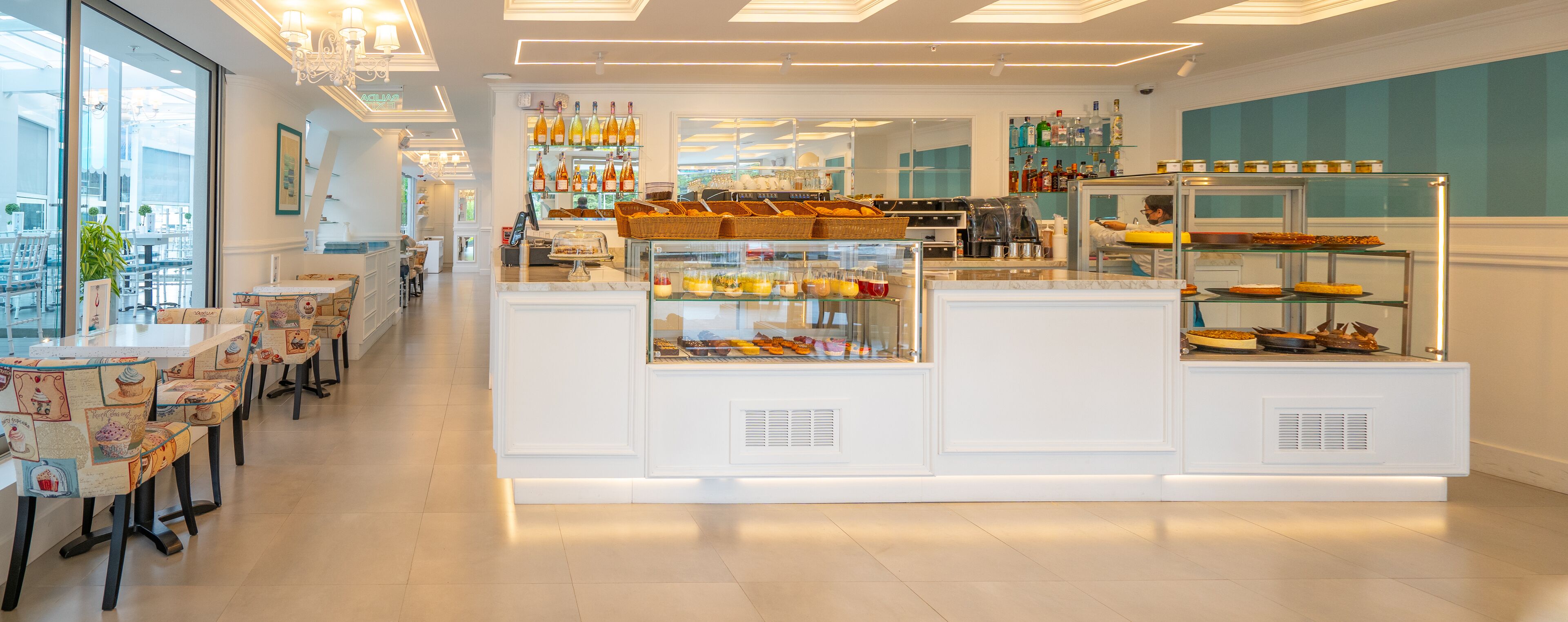 Un café moderne avec un comptoir central où sont exposées des pâtisseries et une machine à café, entouré de tables et de chaises.