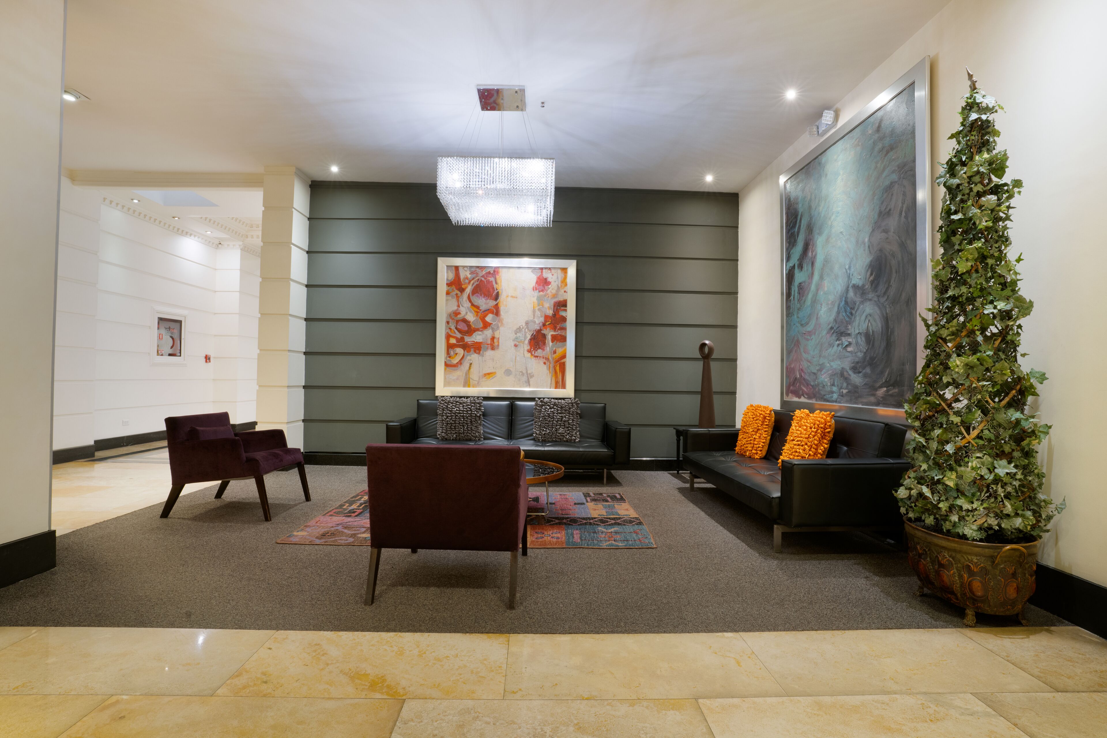 Een moderne lobby met een zithoek, een groot abstract schilderij, een potplant en een kroonluchter.