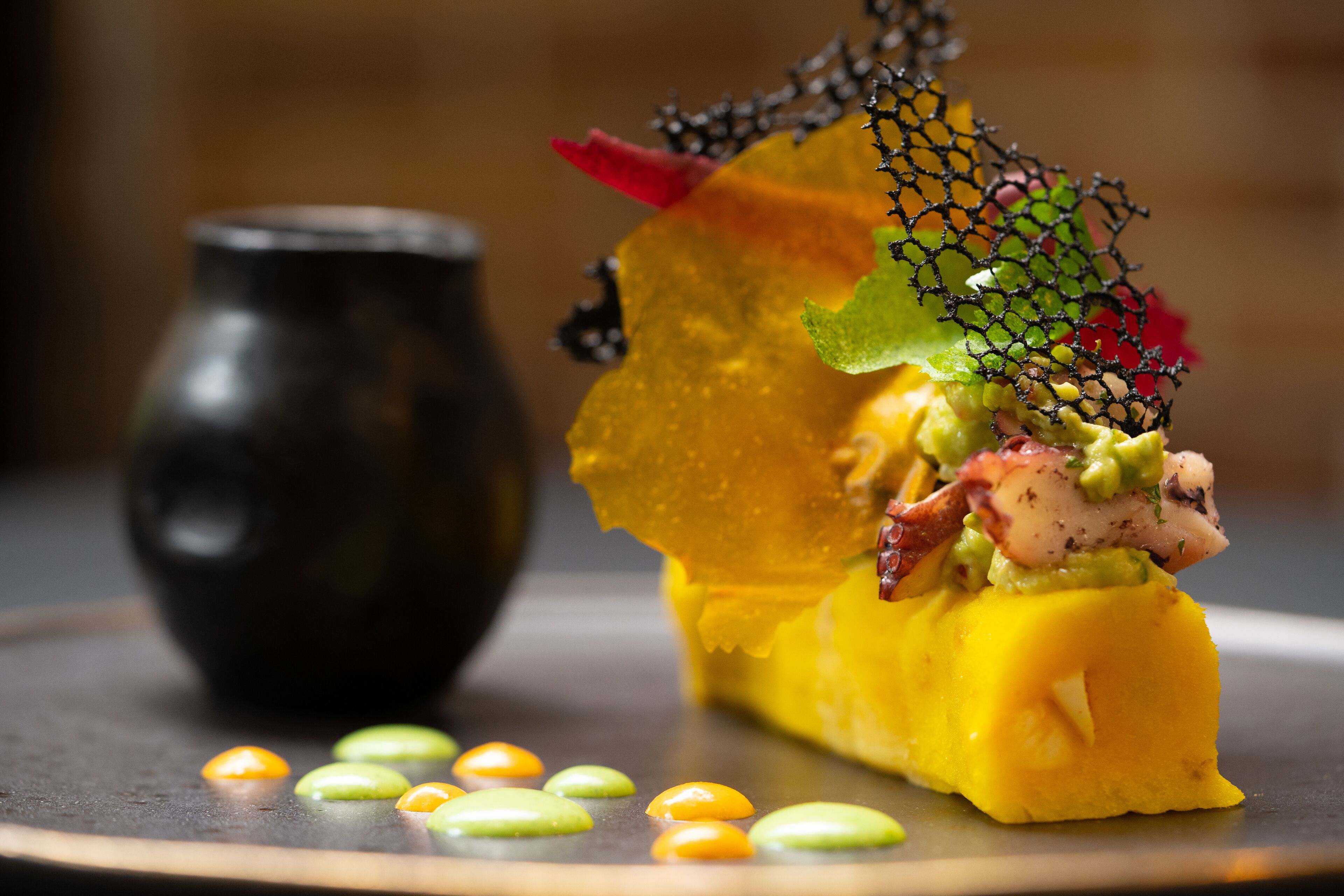 Un postre con base amarilla, esferas verdes y anaranjadas, y una red decorativa en la parte superior.