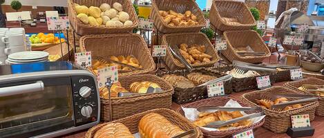 A buffet with various bread and pastries displayed in wicker baskets, a toaster, and a coffee station.