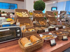 Buffet com diversos pães e pastelaria expostos em cestos de vime, torradeira e estação de café.