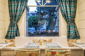 Un comedor con vista a un edificio a través de una ventana, cortinas a rayas y una mesa cubierta con un mantel a rayas y varios objetos.