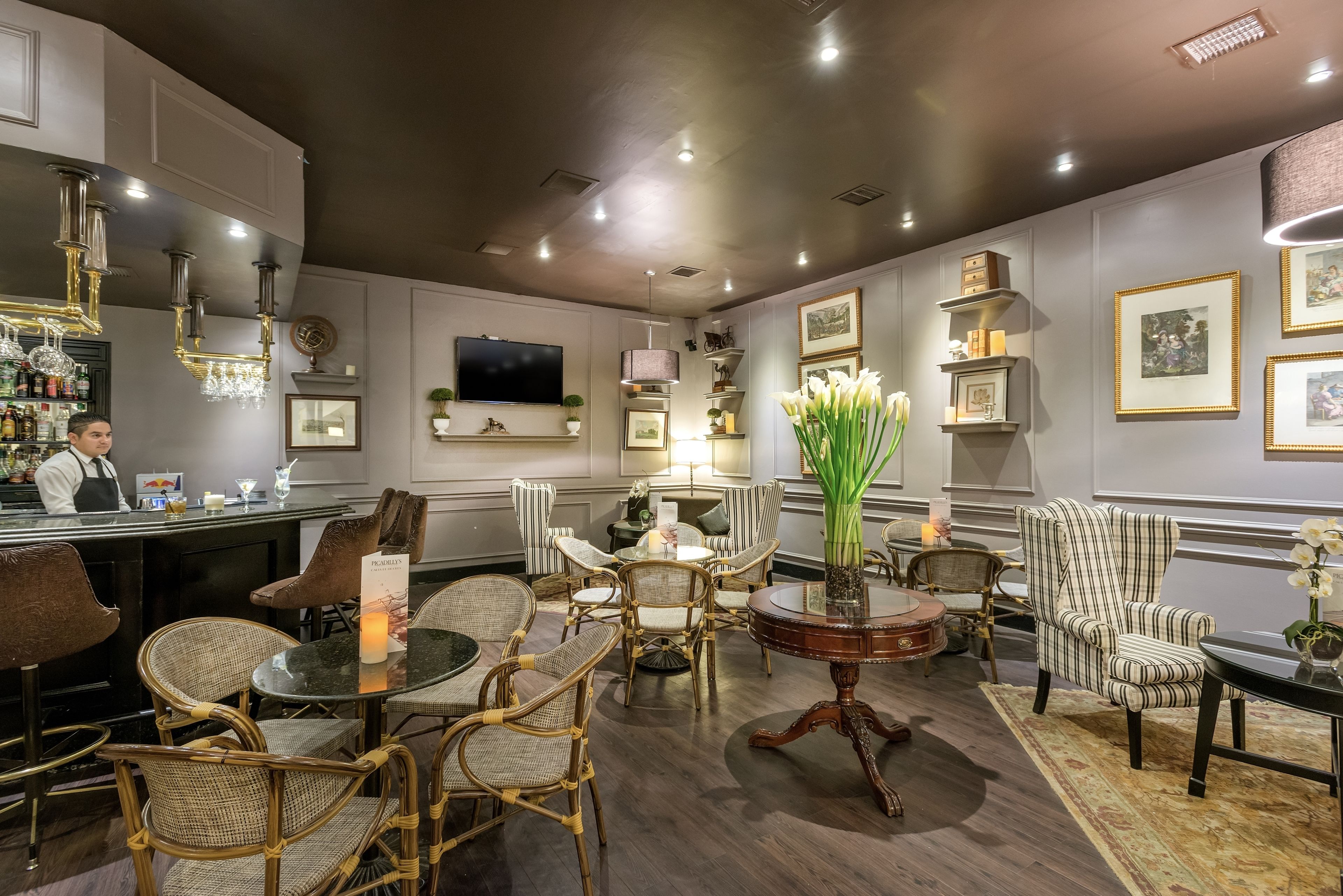 A well-lit, elegantly furnished lounge area with wicker chairs, a round table, and a bar counter.