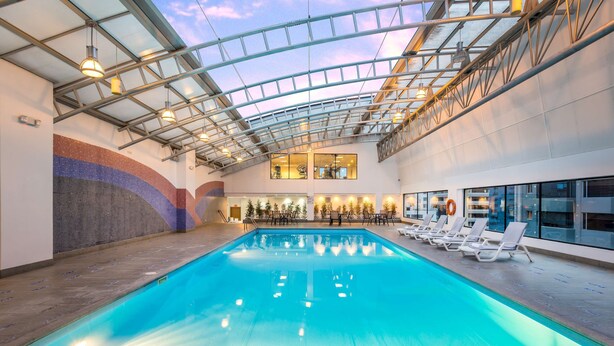 Una piscina interior con techo de cristal, sillas de descanso y vistas a la ciudad.