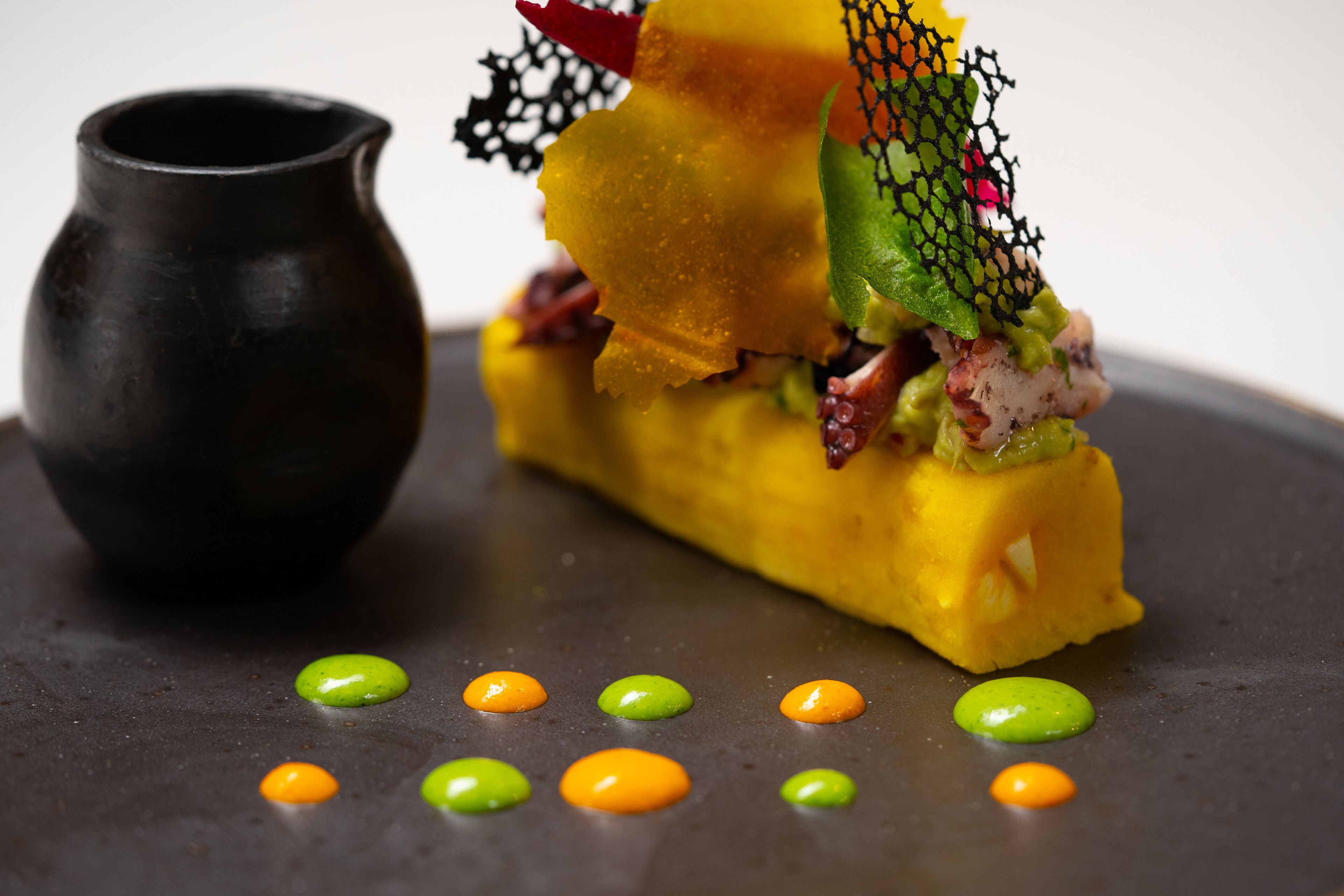 A dessert with a unique presentation, including a small black pitcher and colorful dots on the plate.