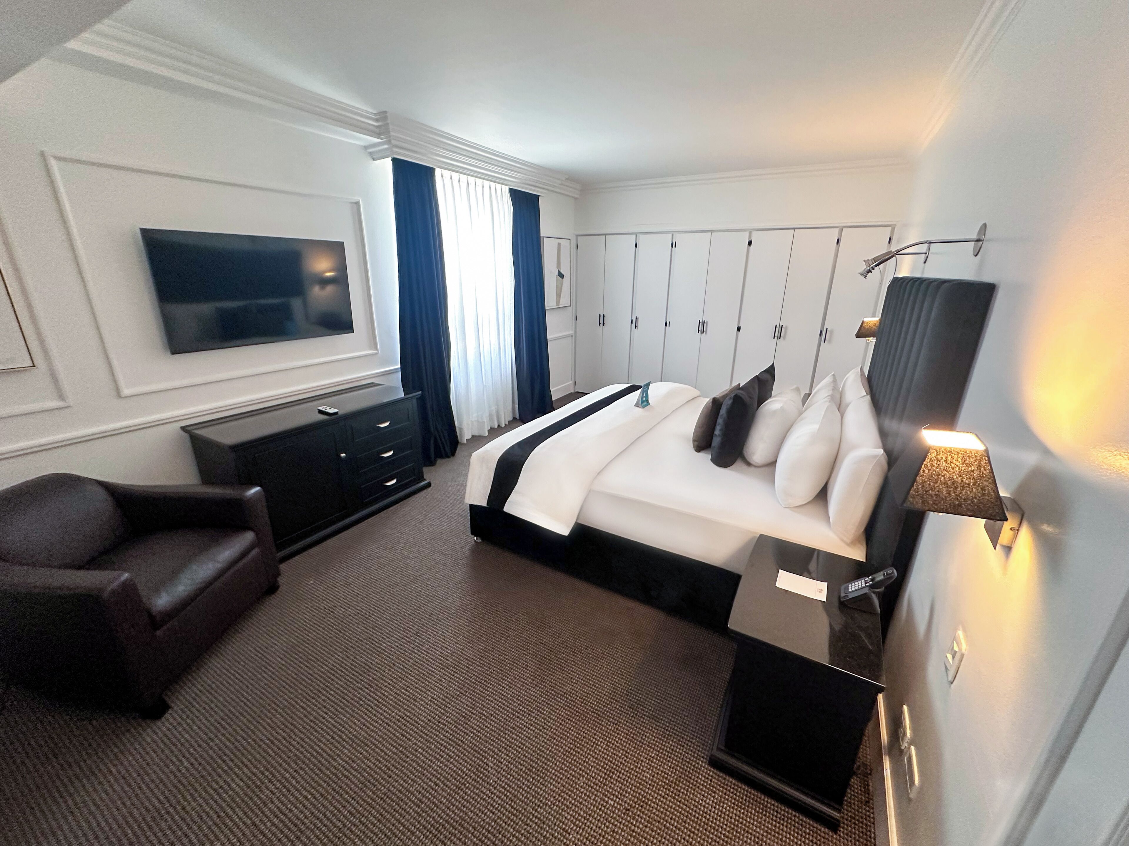 Ein Hotelzimmer mit Bett, Fernseher, Schreibtisch und Kleiderschrank.