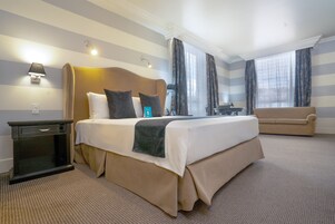 Une chambre d’hôtel avec un grand lit, une table de chevet, une commode, un canapé et une fenêtre avec des rideaux.
