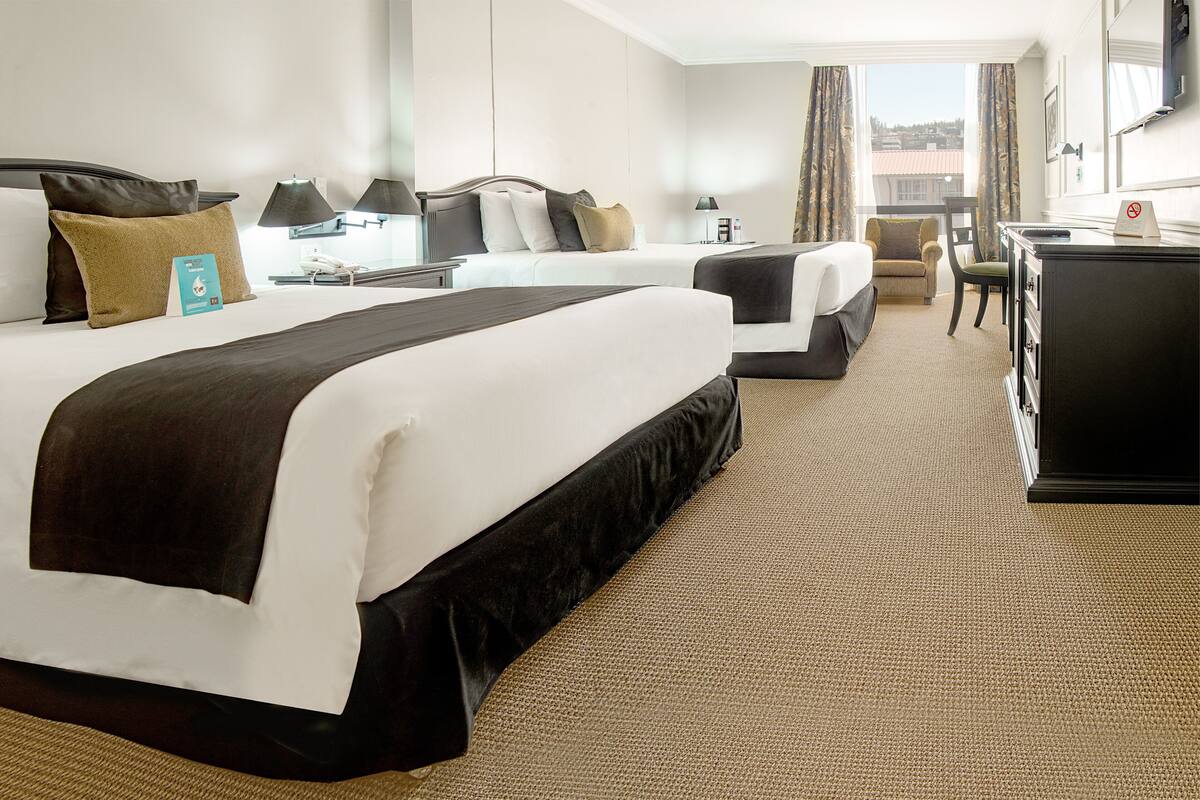 A hotel room with two beds, a desk, and a chair.