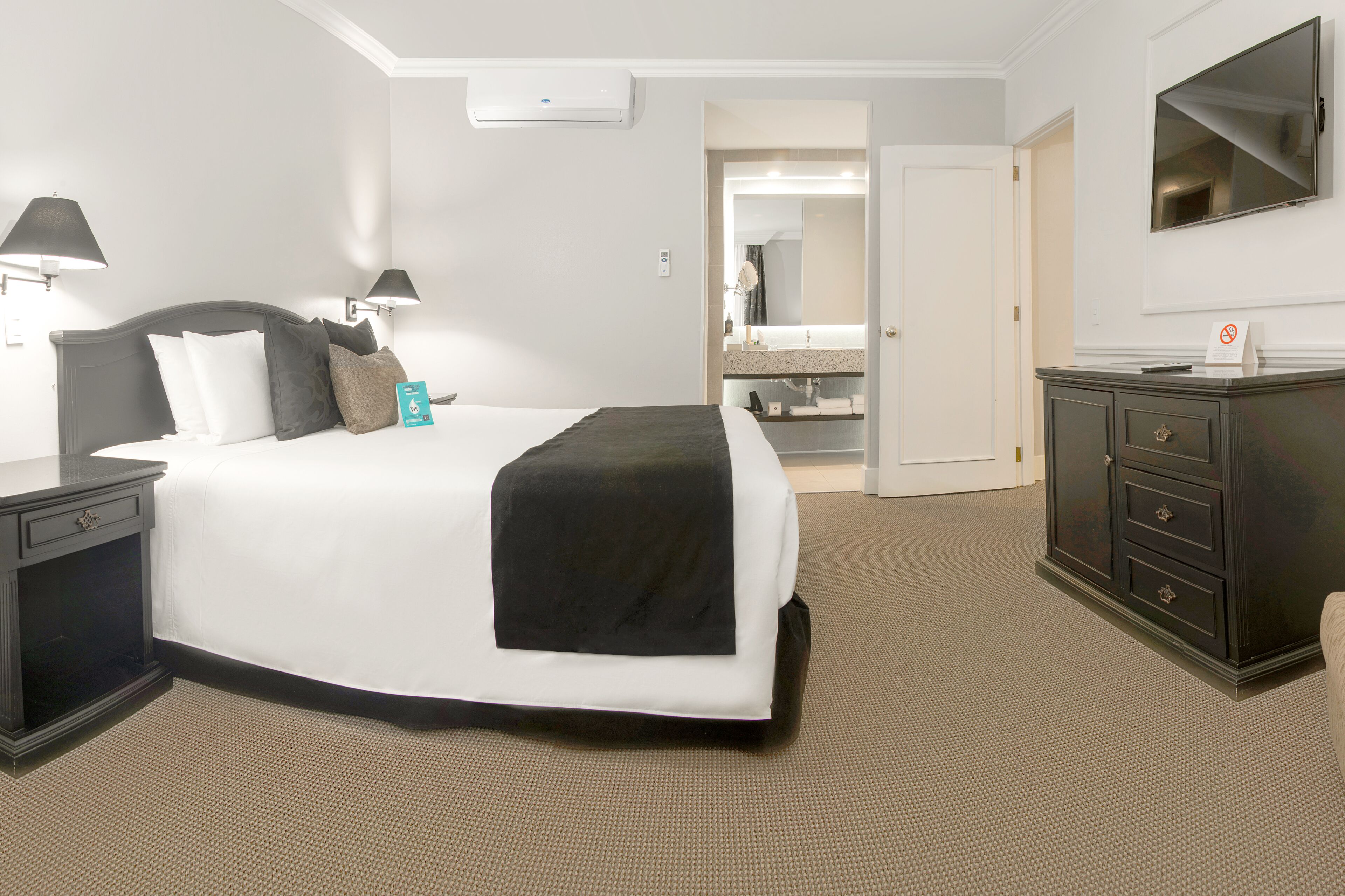 A hotel room with a bed, bedside tables, a dresser, a mirror, and a TV.