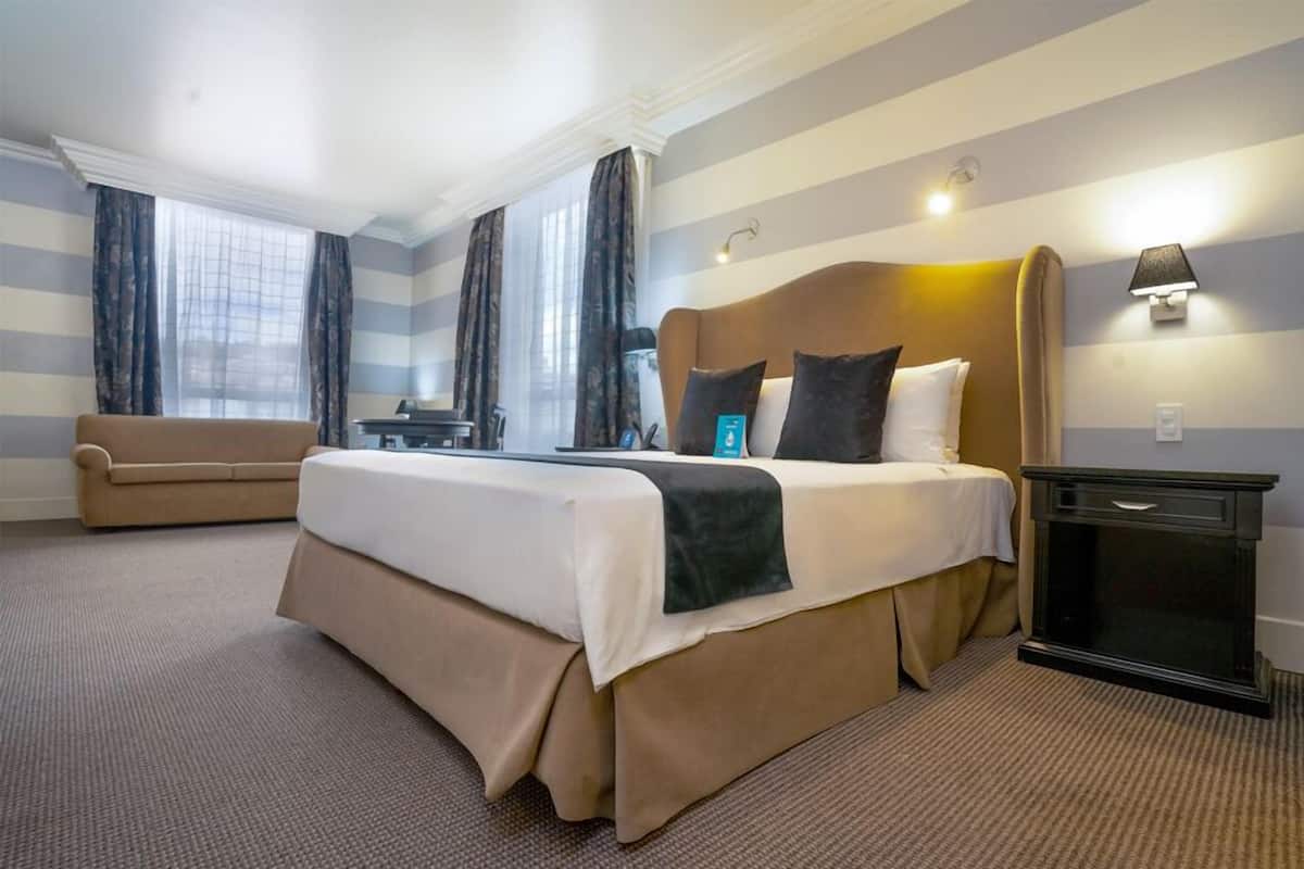 A hotel room with a large bed, a sofa, a desk, and a lamp.