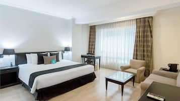 Habitación de hotel con una cama grande, un escritorio, una silla, un sofá y una mesa de centro.