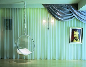 A room with a hanging chair, a framed picture on the wall, and a curtain with a draped fabric.