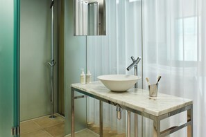 A modern bathroom with a large white sink, a mirror, and a shower area.