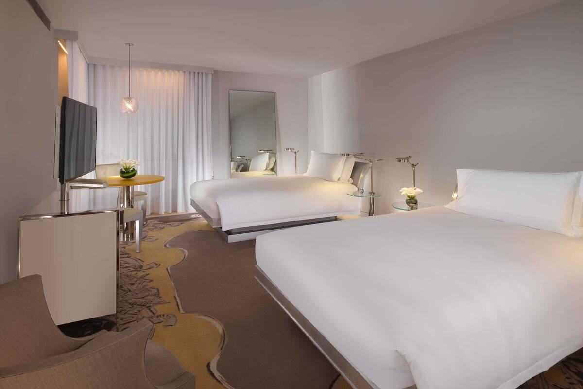 Une chambre d’hôtel avec deux lits, un bureau, une chaise, une télévision et un miroir.