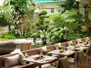 An outdoor seating area with tables and benches, surrounded by lush greenery and a variety of plants. - Sanderson London, a Morgans Originals hotel (London)