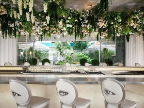 Ein Restaurant mit einer langen Theke, weißen Stühlen und hängenden Blumendekorationen.