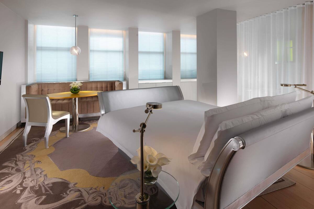 Une chambre d’hôtel moderne avec un grand lit, un bureau avec une chaise et une fenêtre équipée de stores.
