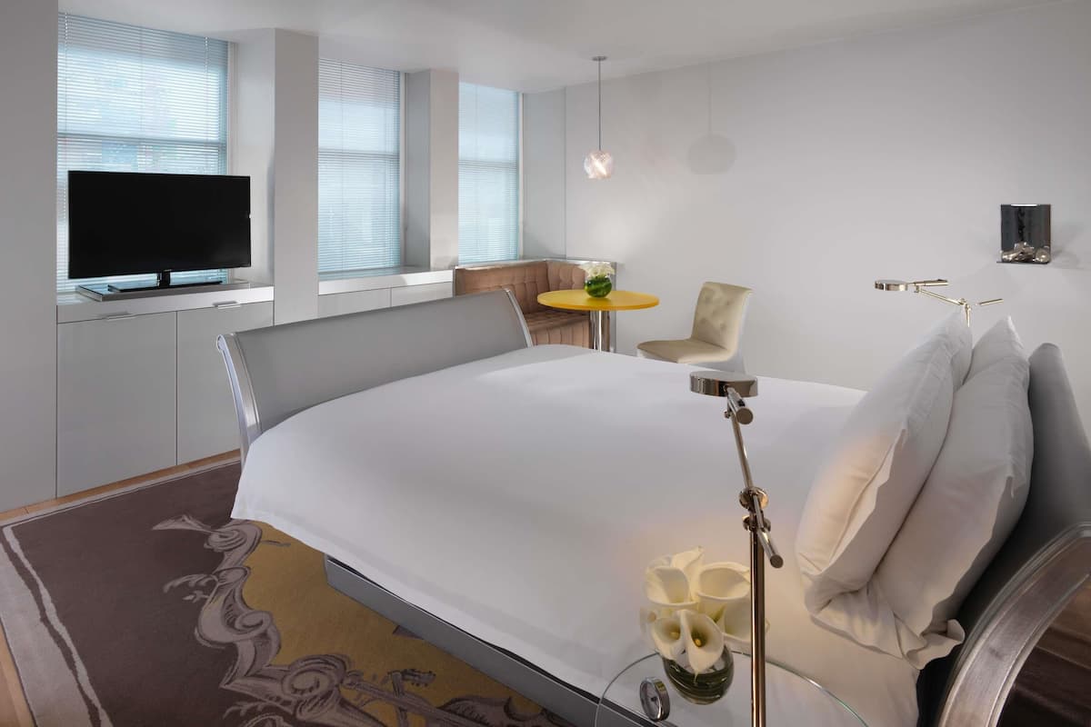 Une chambre d’hôtel moderne dotée d’un grand lit, d’un téléviseur à écran plat, d’une petite table ronde avec une chaise, et d’un vase décoratif avec des fleurs.