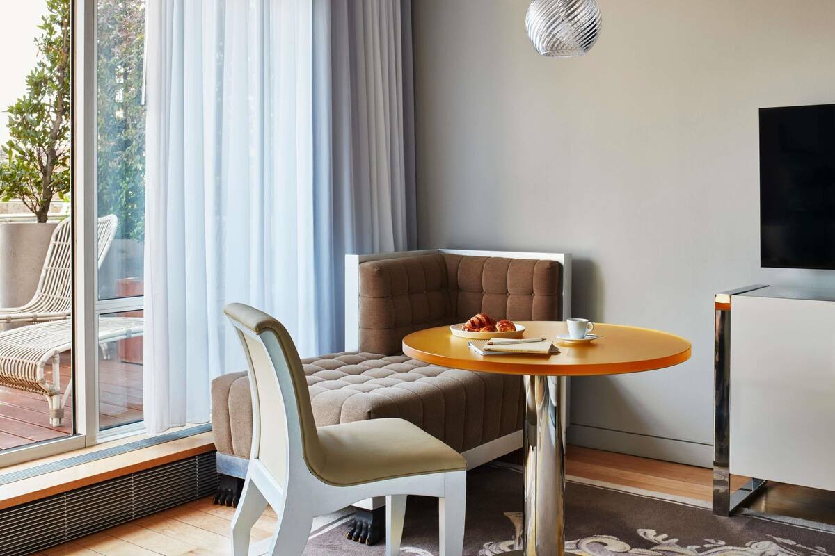 Une chambre moderne avec un canapé, une table ronde, un téléviseur et une vue sur l’extérieur.