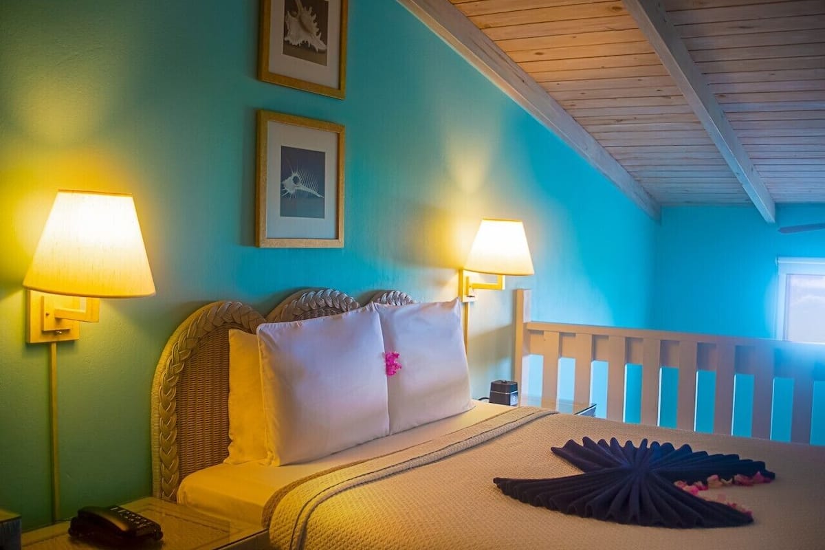 Une chambre d’hôtel avec un lit, deux lampes de chevet, une tête de lit en bois, une fenêtre avec vue et une rambarde en bois.