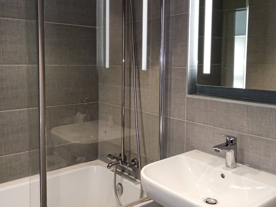 Un baño moderno con ducha de vidrio, bañera blanca y lavamanos blanco.