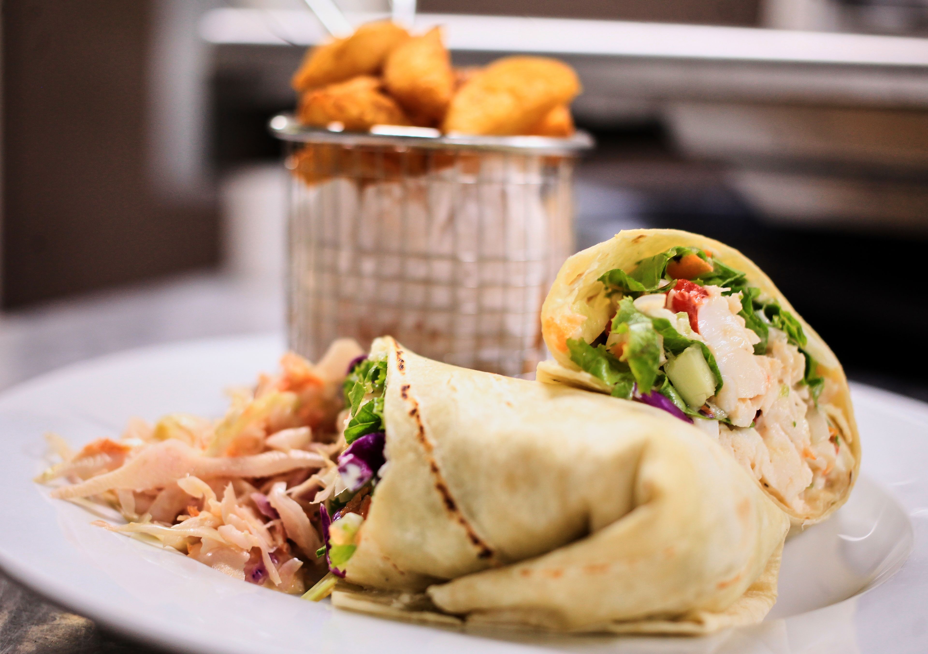 A plate with a wrap sandwich and a side salad, and a basket of fried items in the background.