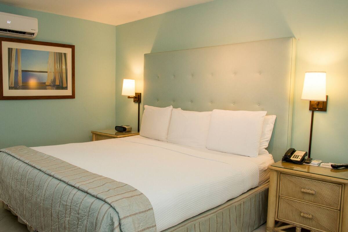 Une chambre d’hôtel équipée d’un lit, de deux tables de chevet, d’une lampe, d’un téléphone et d’un appareil de climatisation.