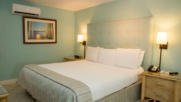 Una habitación de hotel con una cama, mesitas de noche, una lámpara, un teléfono y un aire acondicionado.
