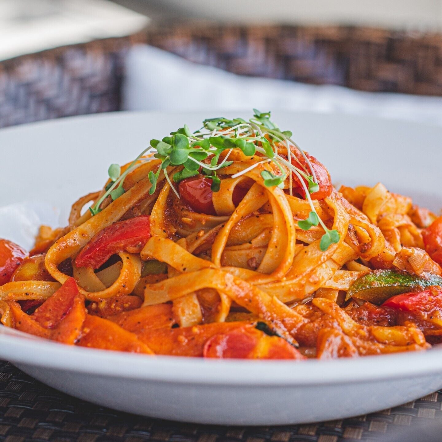 A bowl of pasta with vegetables and sprouts on a white plate.