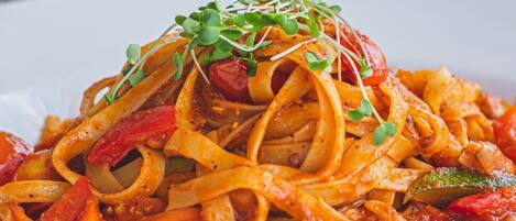 A bowl of pasta with vegetables and sprouts on a white plate.