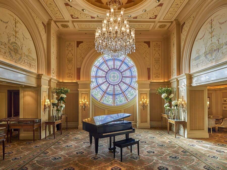 A grand room with a grand piano, a large stained glass window, and ornate wall decorations.
