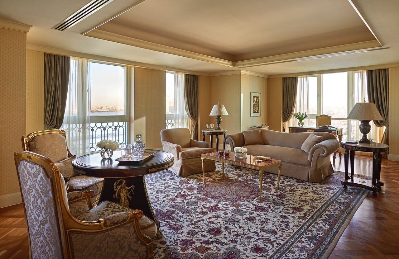 A spacious living room with a large window, a round coffee table, and a patterned rug.