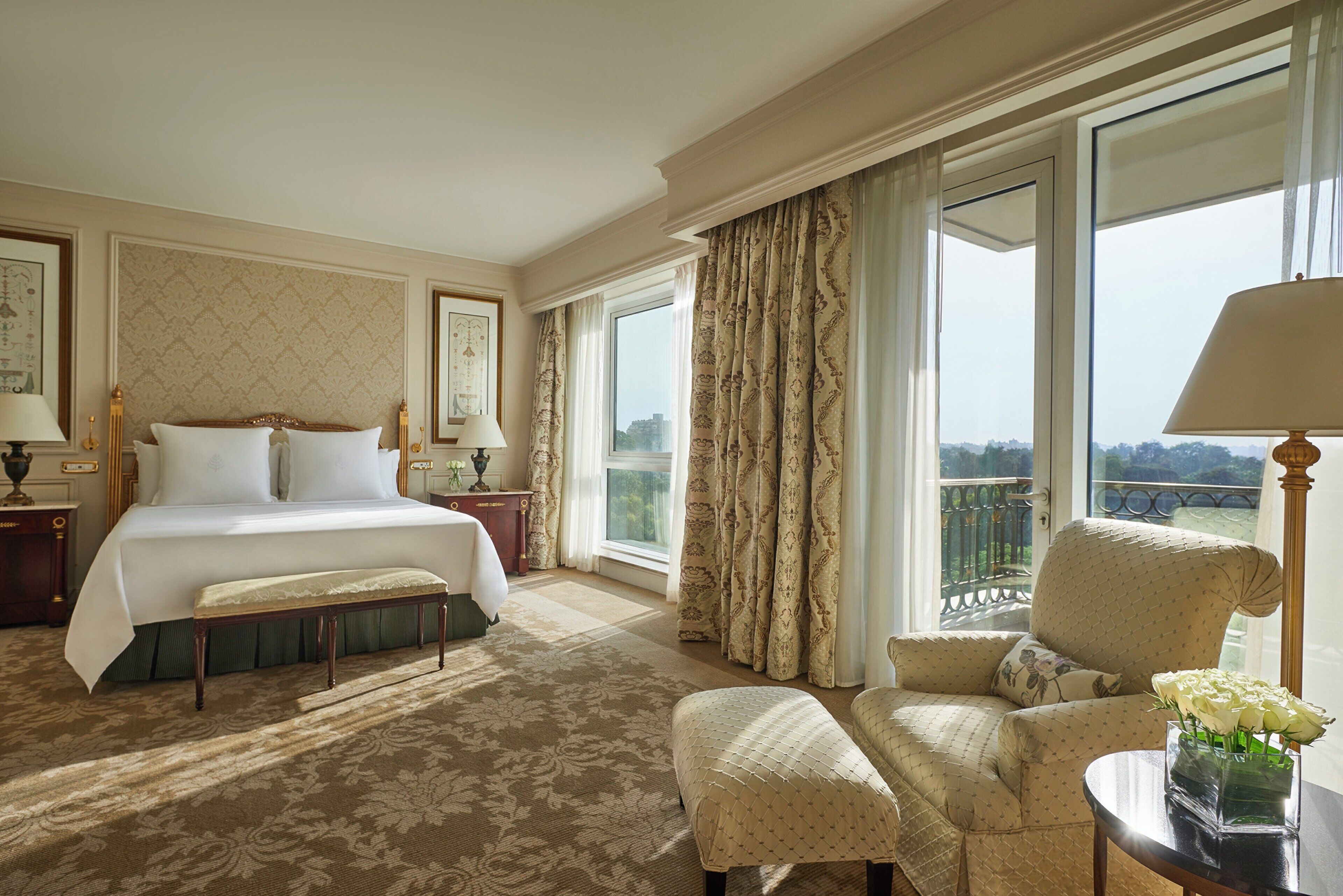 Una habitación de hotel con una cama grande, una zona de estar con una silla y una mesa, y un balcón con vistas.