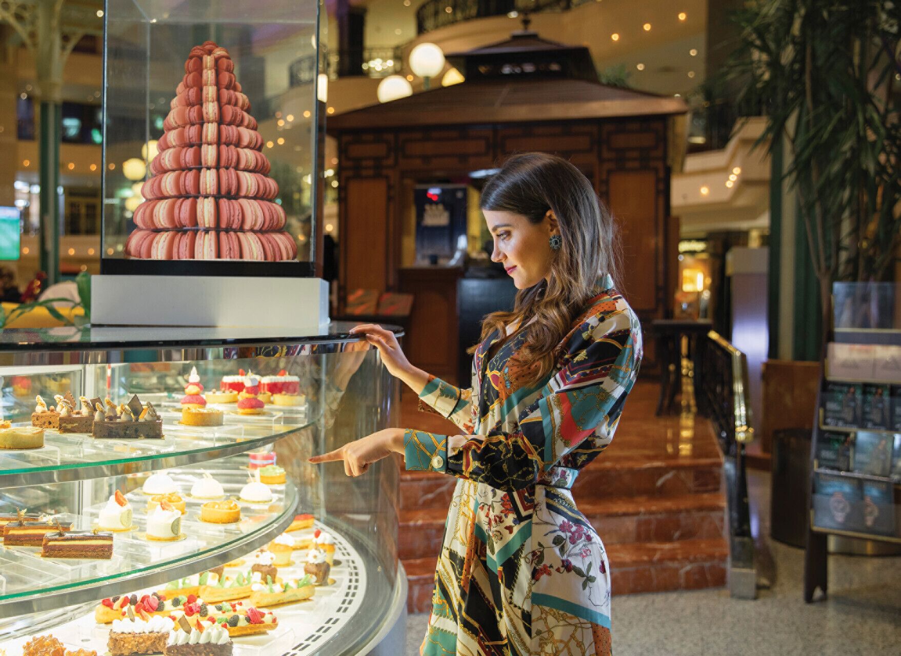 Una mujer con un vestido estampado señala un mostrador de postres en un hotel.
