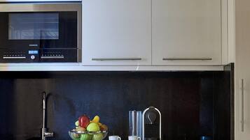 Una cocina moderna con microondas de acero inoxidable, un frutero, cafetera y un lavamanos.