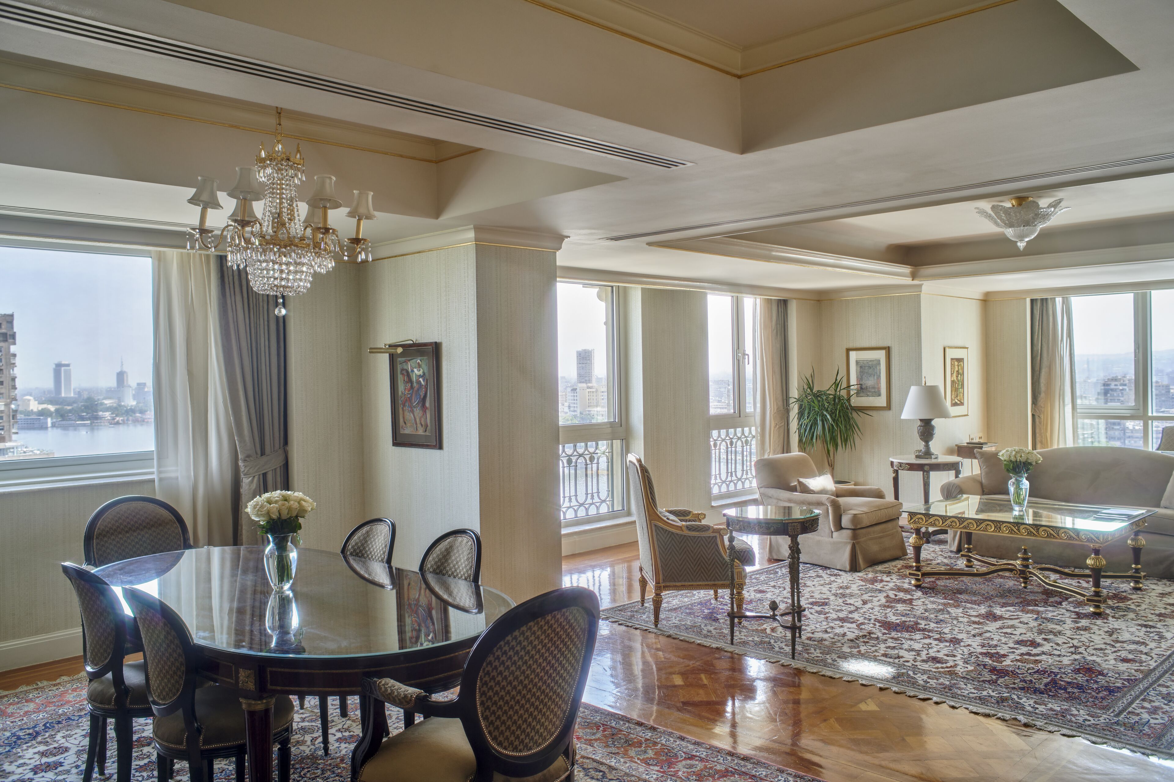 A spacious living room with a large window, a chandelier, and a dining area with a table and chairs.
