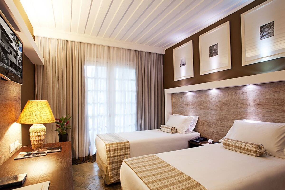 Una habitación de hotel con dos camas, una mesita de noche, una lámpara y un televisor montado en la pared.