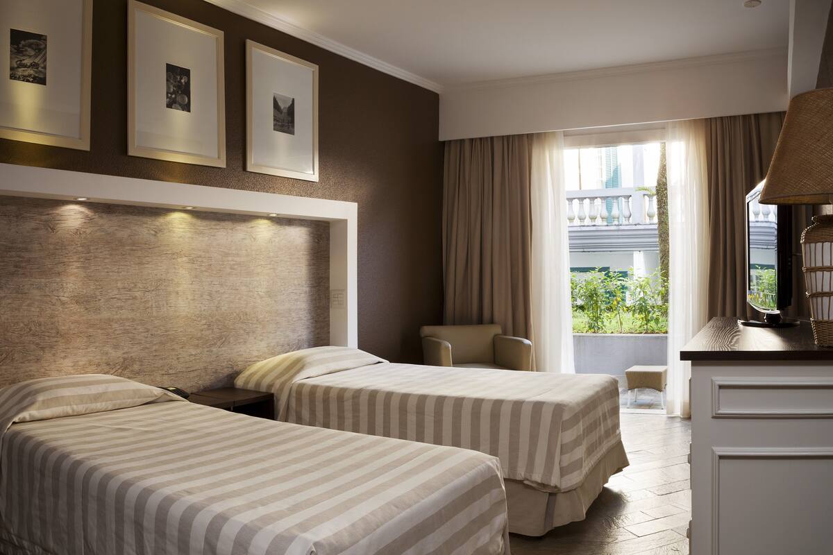 Habitación de hotel con dos camas, un escritorio, una silla y un ventanal con cortinas.