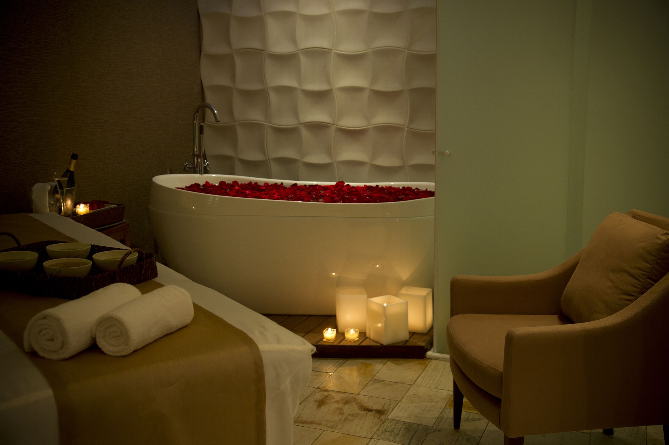 Une salle de spa dotée d’une baignoire remplie de pétales de rose, d’un fauteuil de massage et de bougies.