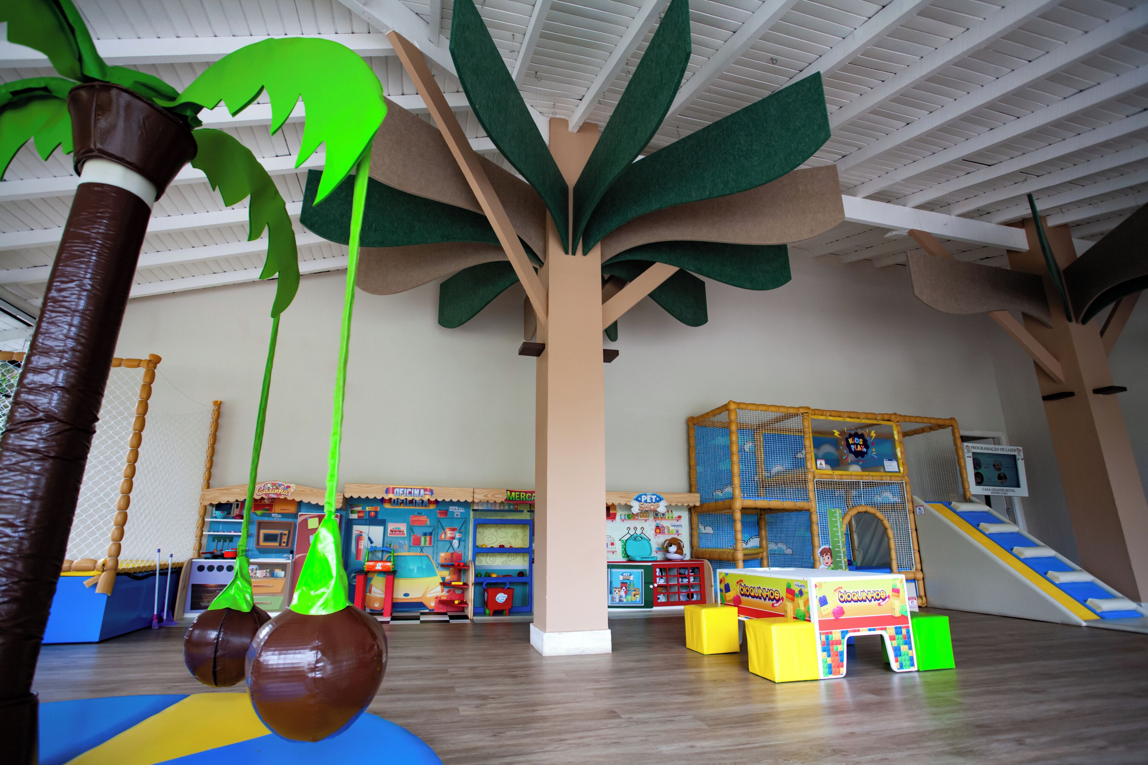 Zona de juegos infantiles con una gran decoración de árbol, estructuras de juego y una tienda de juguetes.