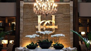 Een modern interieur met een grote kroonluchter, een logo dat aan de muur hangt, en potplanten.