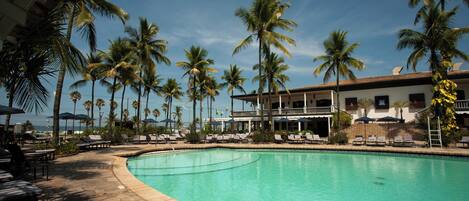 A pool area with lounge chairs, palm trees, and a building with a balcony.
