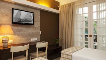 Habitación de hotel con televisión montada en la pared, escritorio con sillas, cama con cubrecama a cuadros y ventana con cortinas.