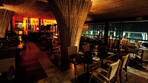 Een restaurant met een bamboeplafond, houten meubels en uitzicht door grote ramen.
